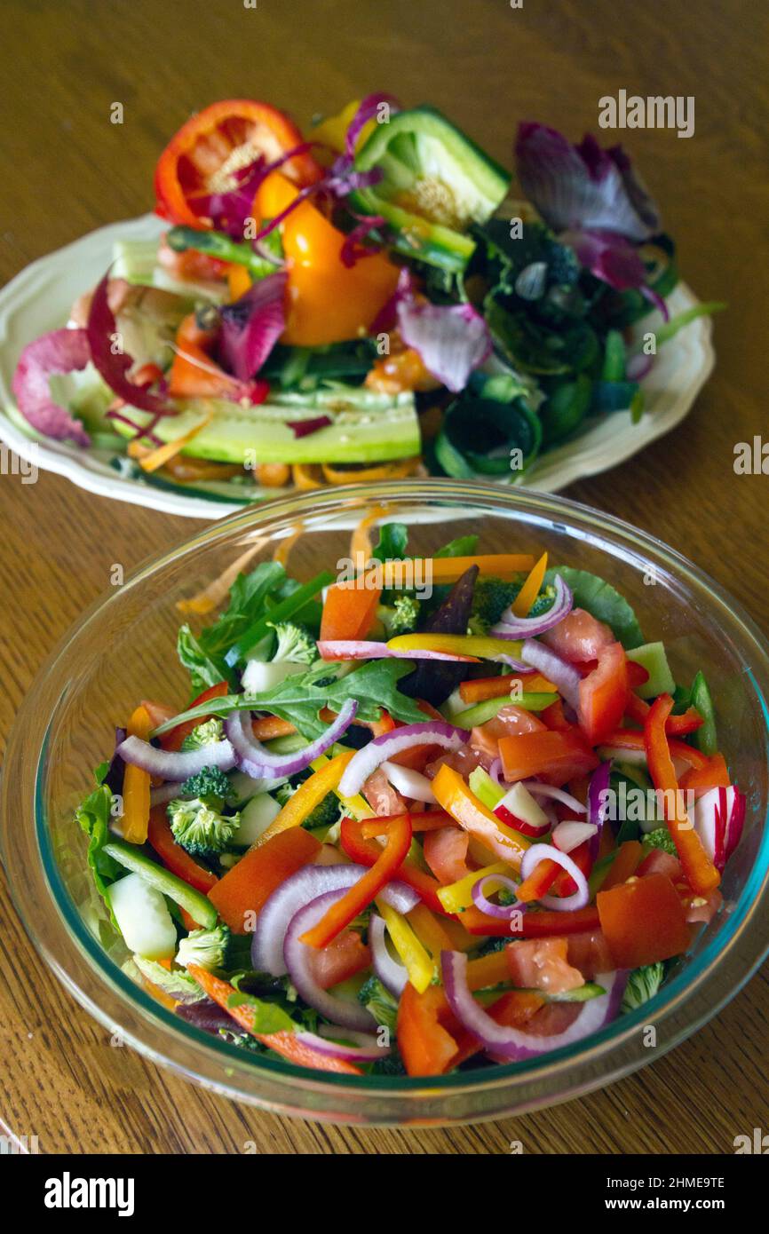A large, summer salad in a glass bowl sits next to an equally large platter overflowing with the wasted peelings and discarded vegetable scraps from m Stock Photo