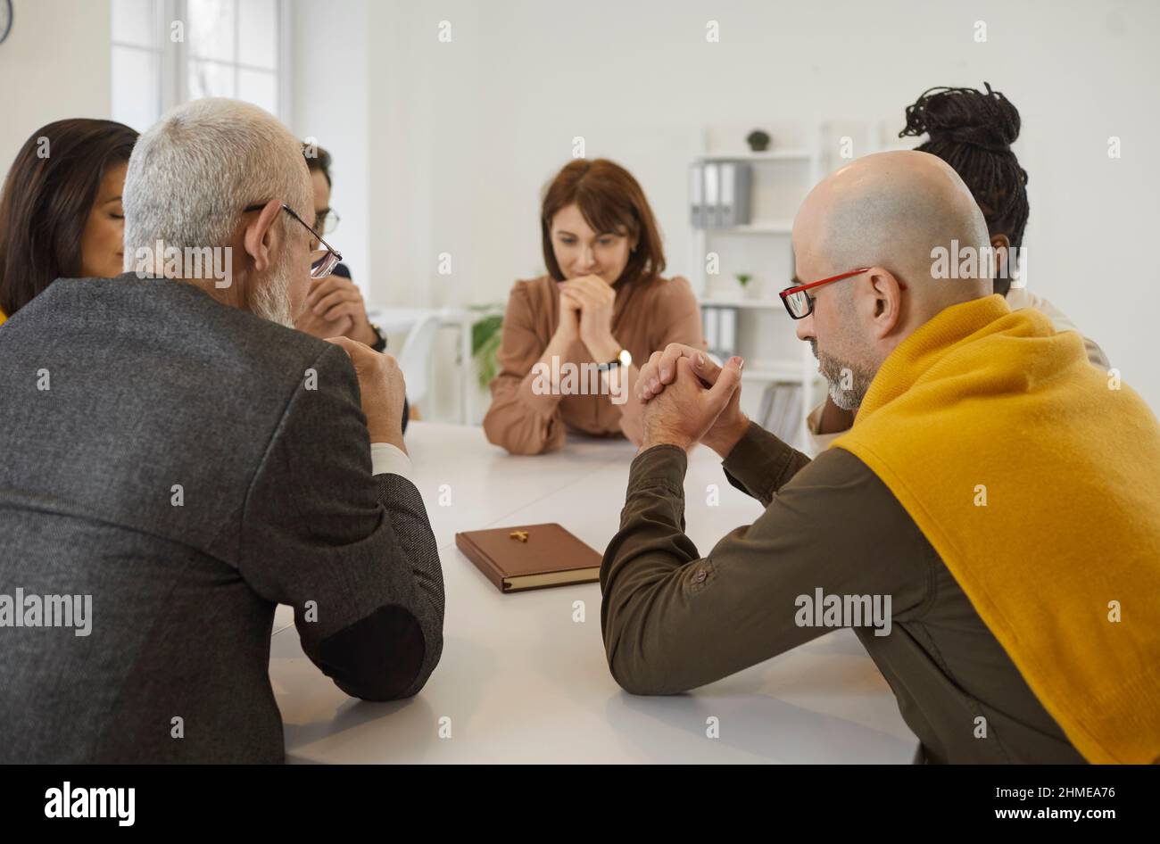 Group of people sitting together around table with Holy Bible and praying to God Stock Photo