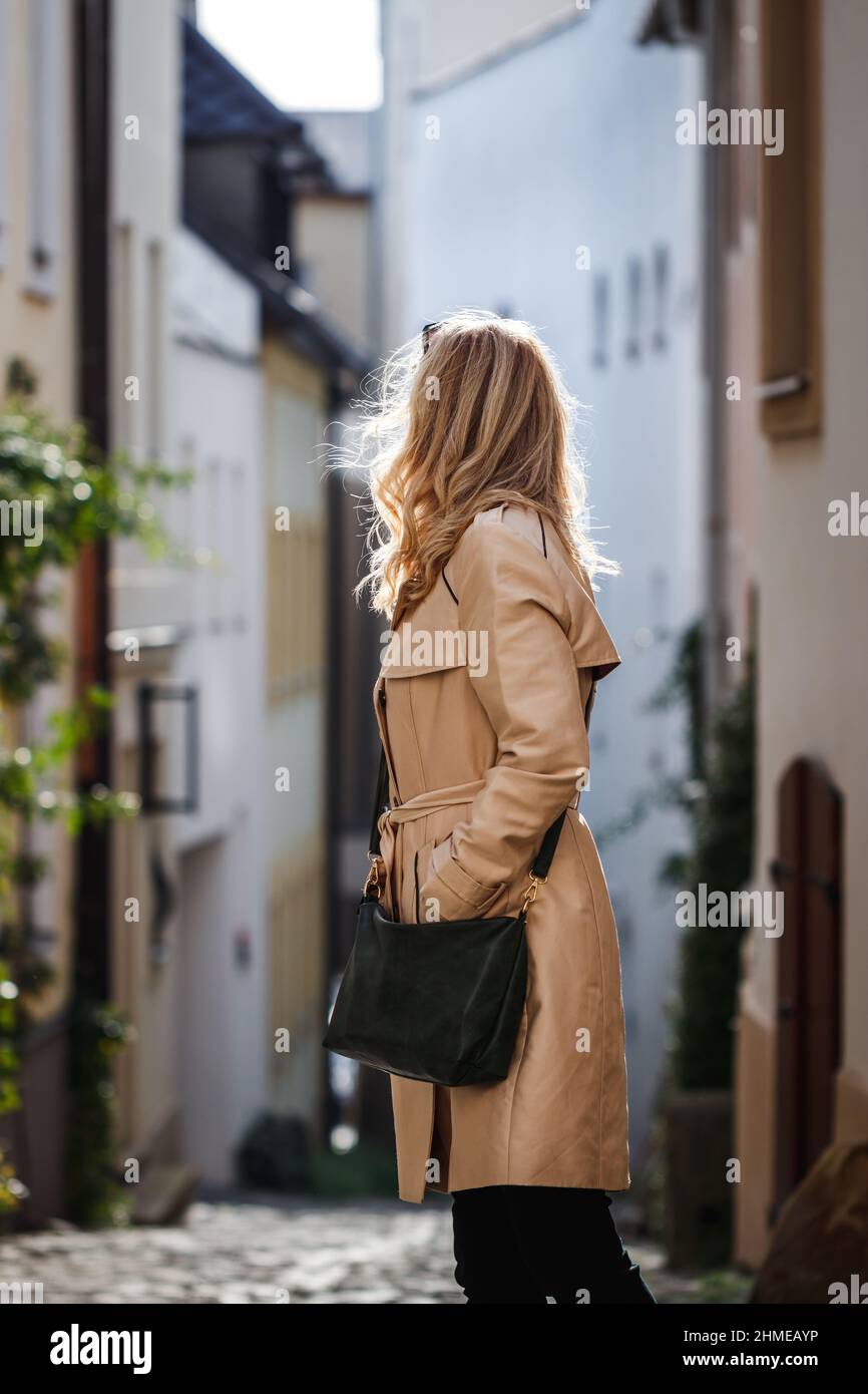 Stylish woman wearing beige trench coat and walking on city street ...