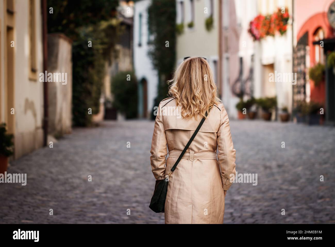 Stylish woman wearing trench coat and walking on city street ...