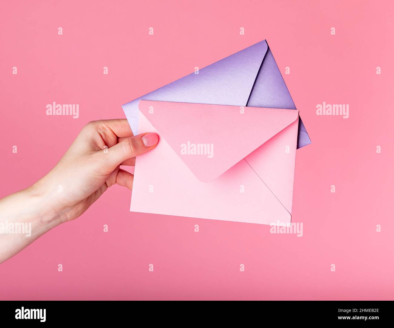 Hand holding envelopes with Valentines day greeting or gift certificates on pink background. High quality photo Stock Photo