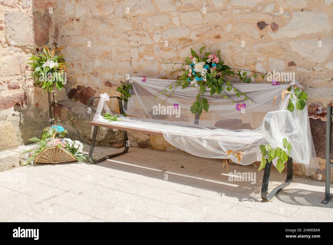 Floral decoration on a bench adorned with flowers and white cloth next to a stone wall outside a church. Stock Photo