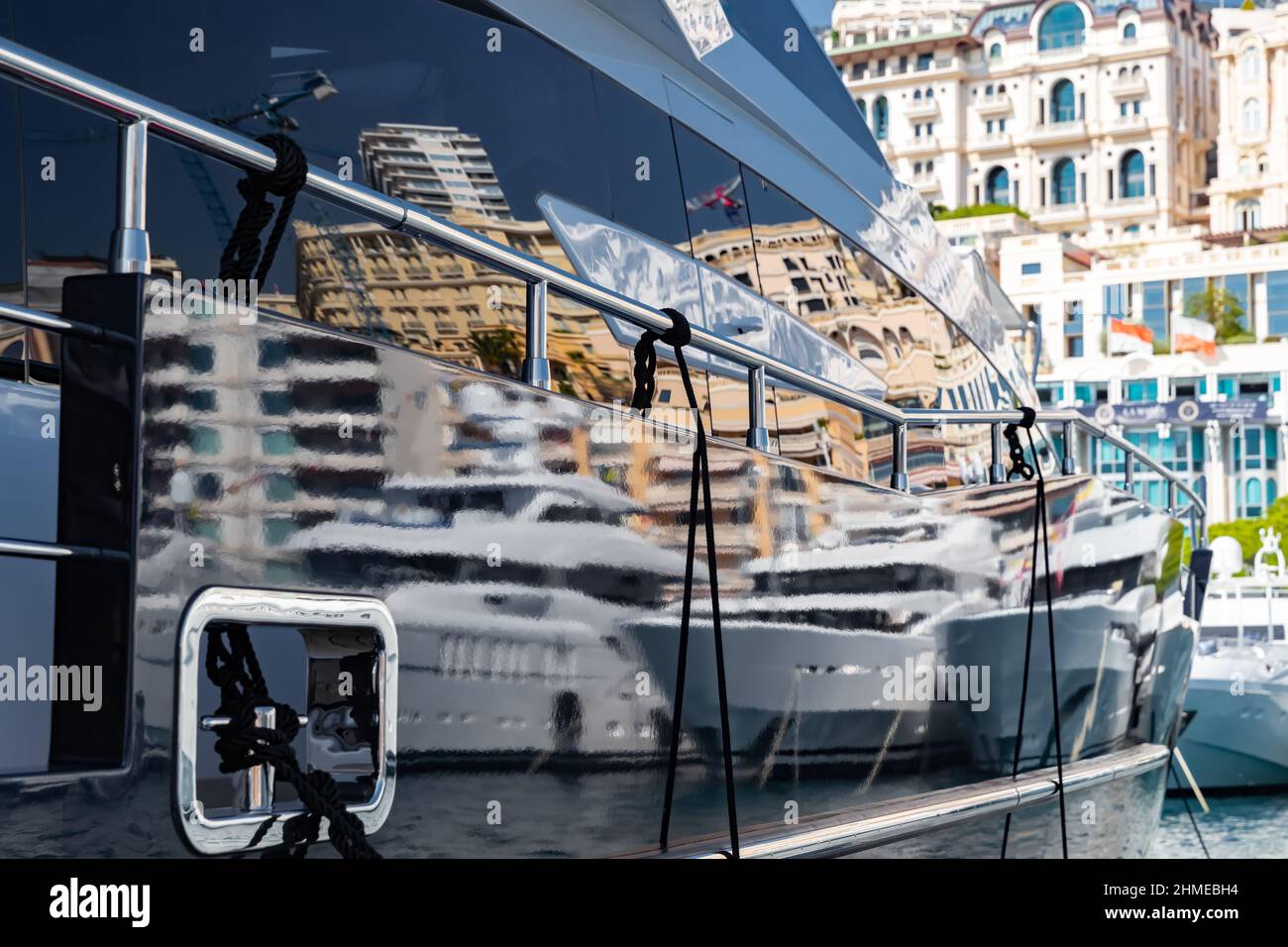 Reflection of a boat and city on a glossy surface of a huge yacht at sunny day, the chrome plated handrail, megayacht is moored in port, are buildings Stock Photo