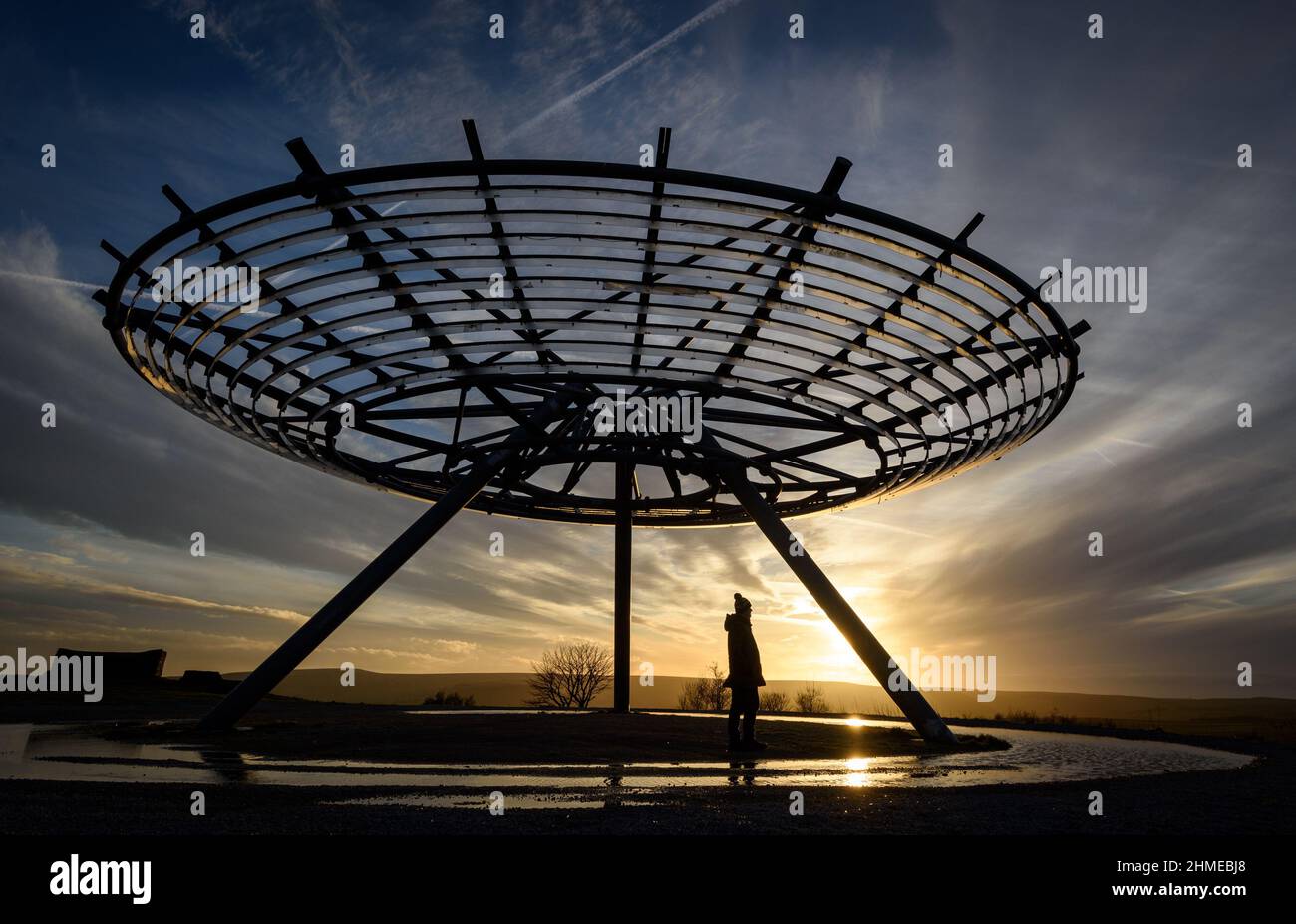 Haslingden, Lancashire, UK, Wednesday February 09, 2022. A walker stops to admire the setting sun at the Halo panopticon above the town of Haslingden, Lancashire, after a beautiful sunny afternoon. Credit: Paul Heyes/Alamy News Live Stock Photo