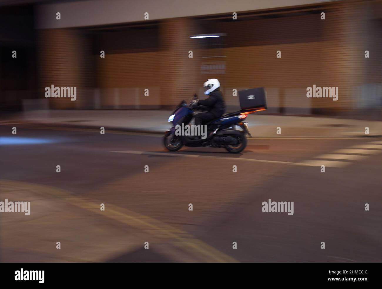 A panning shot with movement with copy space of a food delivery motorbike rider riding at night. Stock Photo