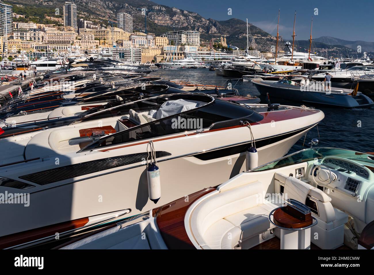 A lot of motor boats in rows are in port of Monaco at sunny day, Monte Carlo, mountain is on background, colourful interior of the boat, are moored in Stock Photo