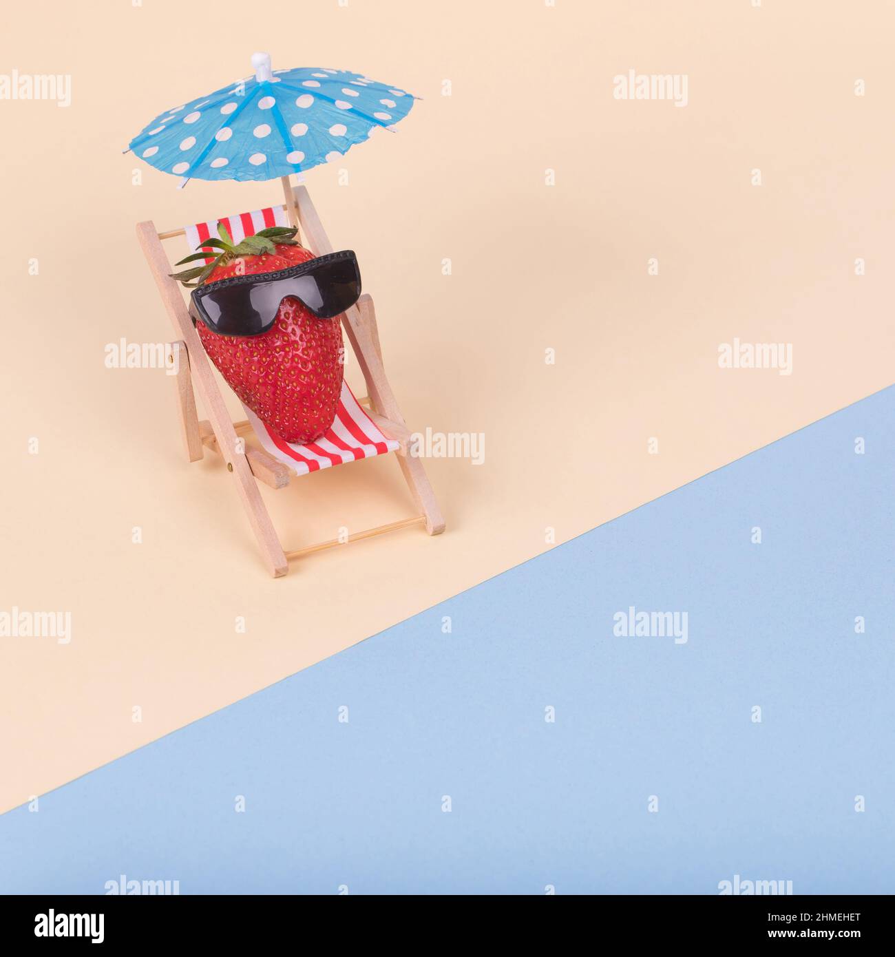 Creative fun idea made of deck chair, sun umbrella and strawberry with sunglasses on a beach. Minimal  summer vacation concept. Stock Photo