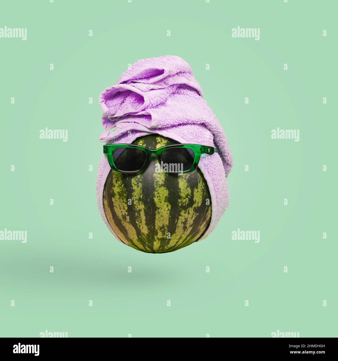 Funny stylish attractive watermelon in sunglasses and a towel on a green background. Minimal tropical summer vacation concept. Stock Photo