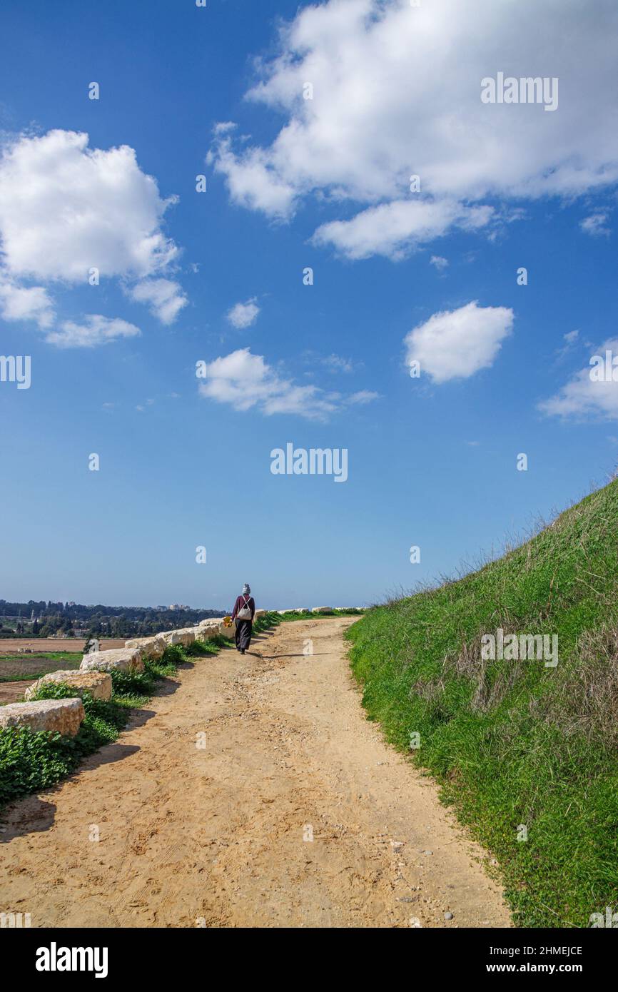 a girl walks along a yellow road up a hill under a blue sky with white clouds Stock Photo