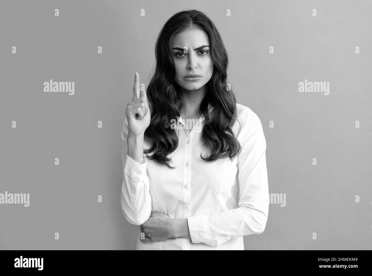 Frown woman executive manager keep finger pointing up grey background, idea Stock Photo