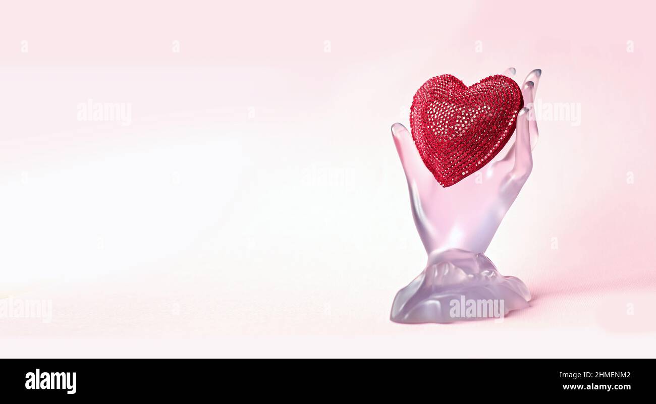 Plastic hand holding a red heart on pink background with copy space ...
