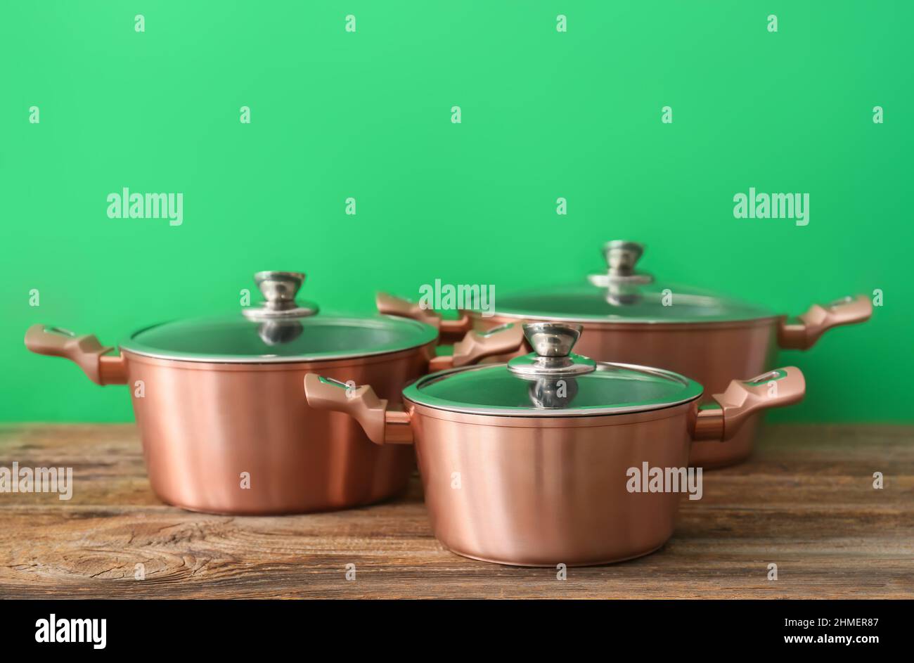 https://c8.alamy.com/comp/2HMER87/copper-cooking-pots-on-wooden-table-against-green-background-2HMER87.jpg