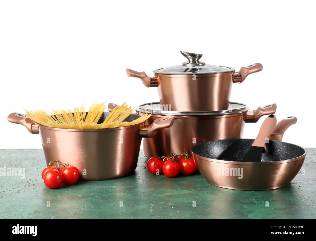Set of copper kitchen utensils with raw spaghetti and tomatoes on green