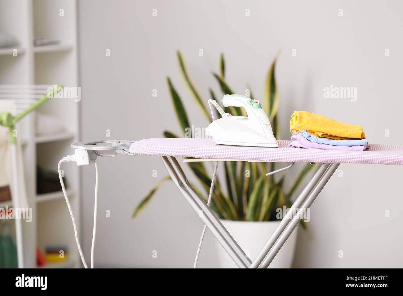 Electric iron and stack of clothes on board Stock Photo