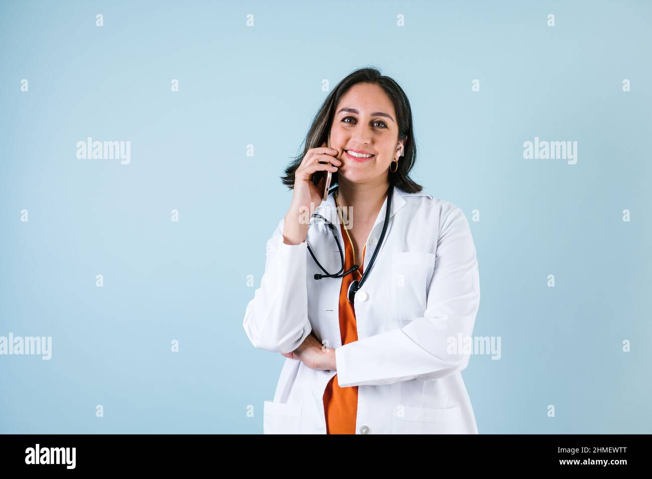 latin doctor woman holding mobile phone over blue background laughing in Mexico Latin America Stock Photo