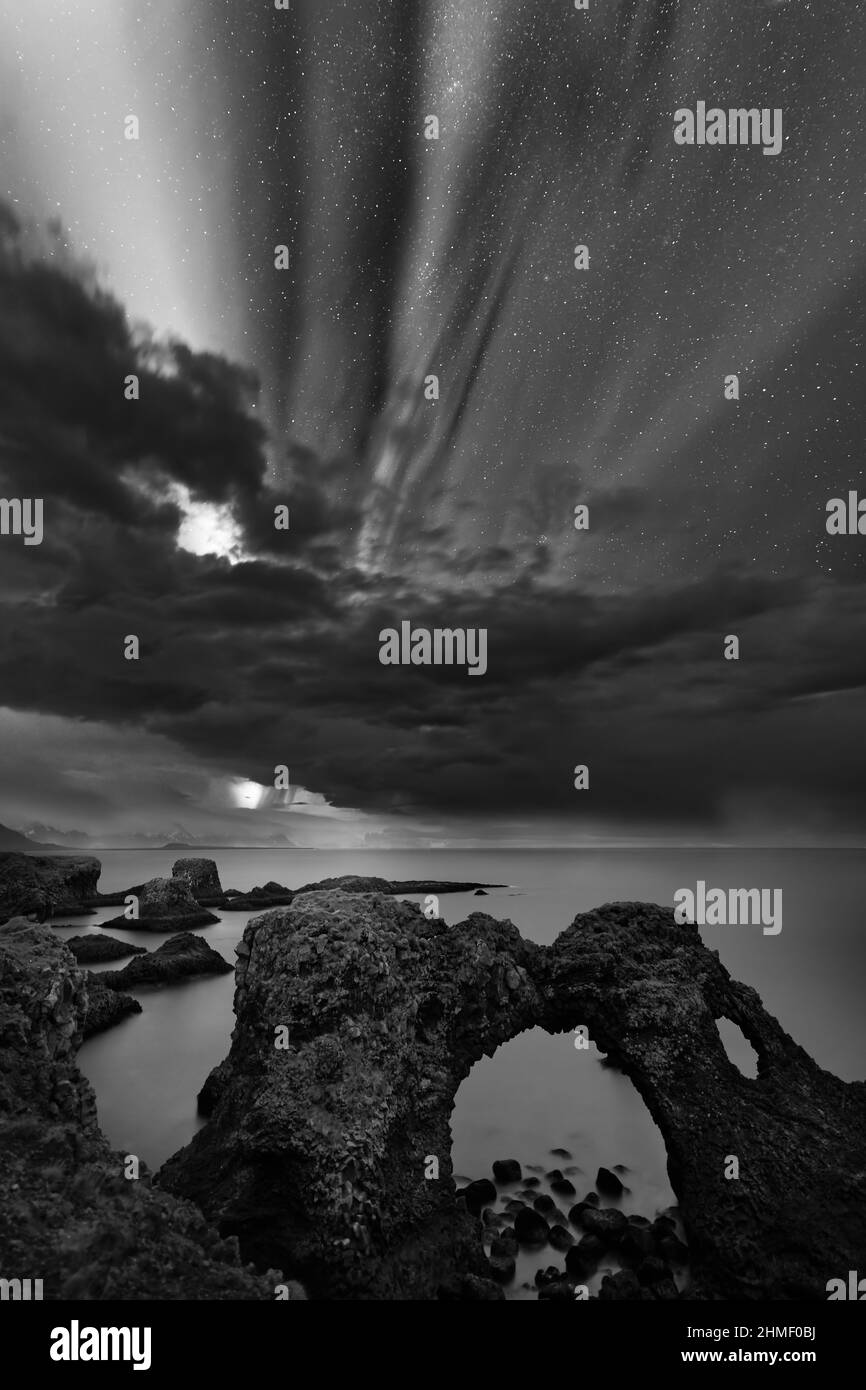 High contrast black and white image of aurora borealis and starry sky above a rock gate on the cliff, some clouds enliven the scene additionally - Loc Stock Photo