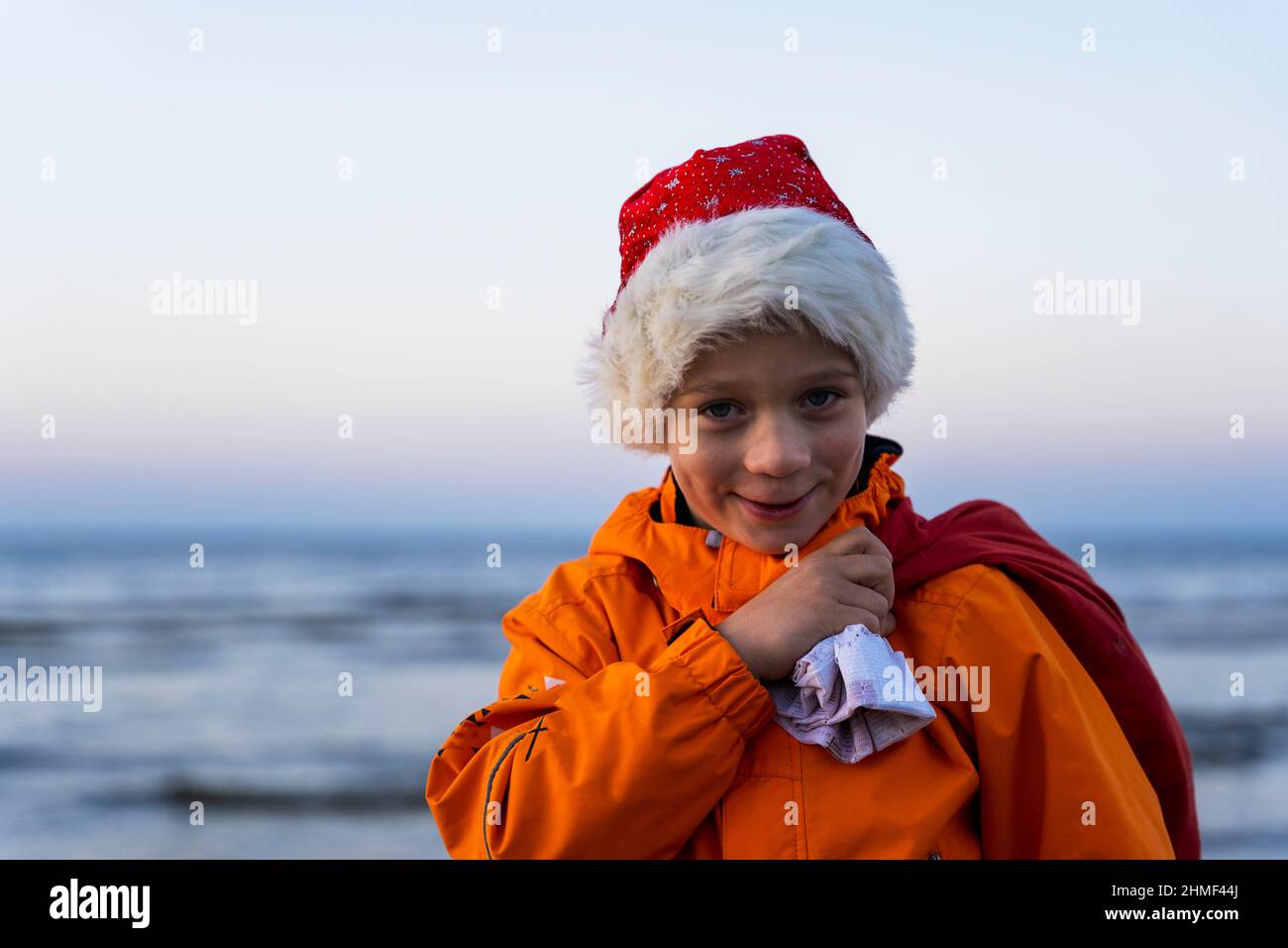 Portrait of a cute boy in a cap of St. Nicholas, with a bag of Christmas and New Year's gifts on the background of the sea, the guy holds a bag of gif Stock Photo