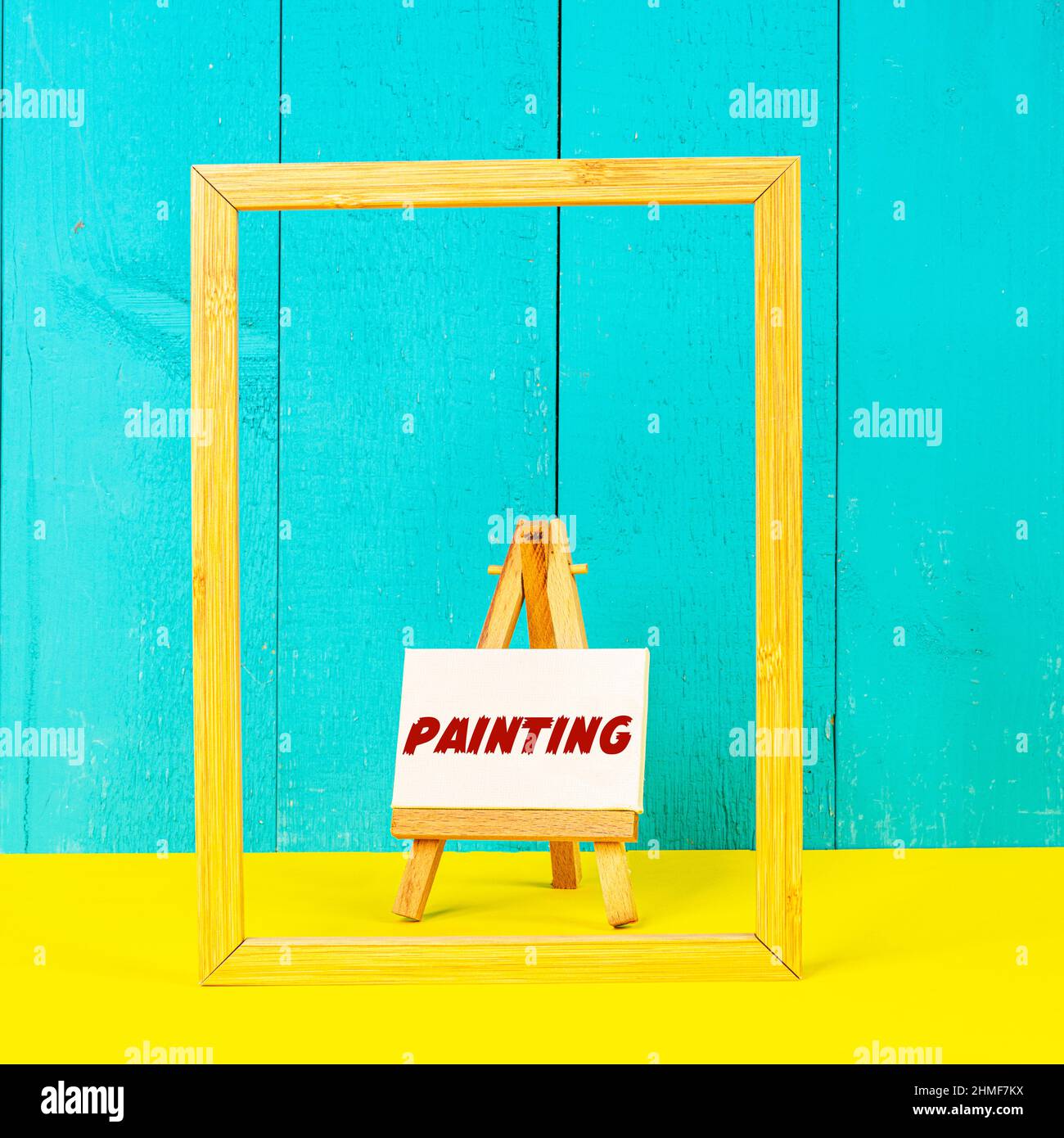 a wooden easel with the word Painting painted on a white canvas Stock Photo