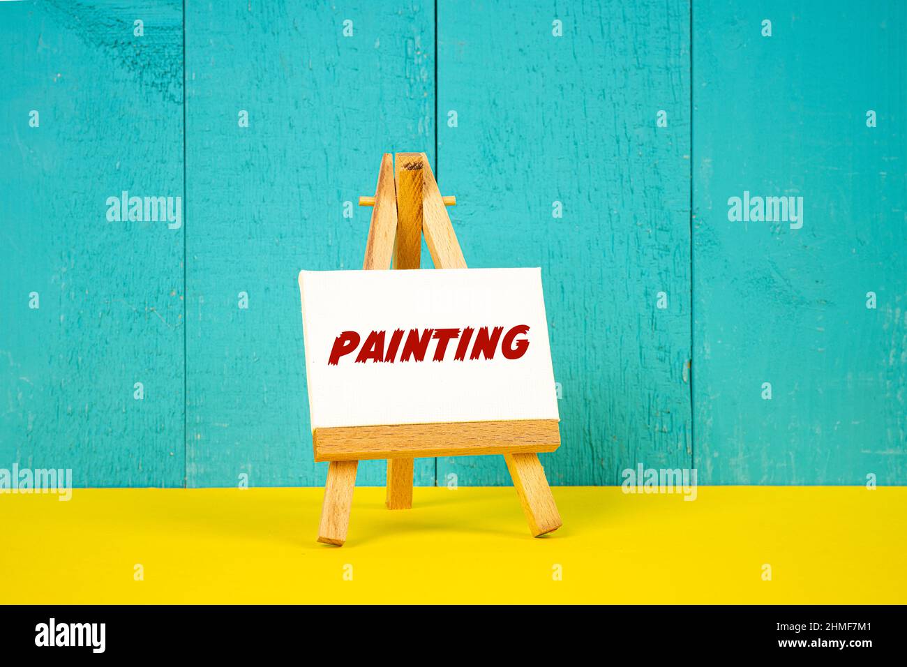 a wooden easel with the word Painting painted on a white canvas Stock Photo