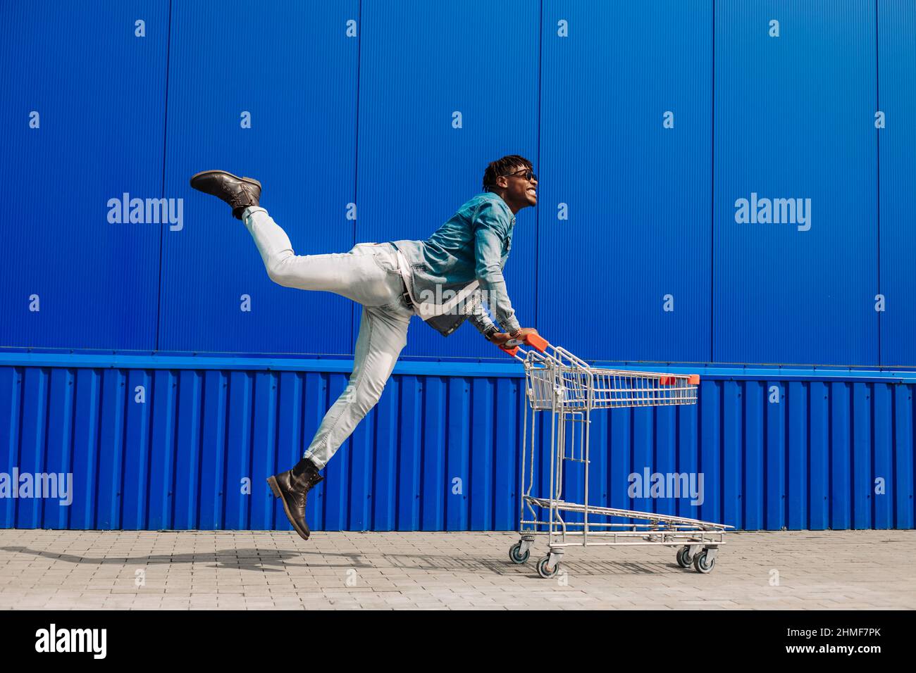 Excited african american man having fun while shopping, man pushing shopping cart in mall. Black man pushing a shopping cart, looking at the camera an Stock Photo