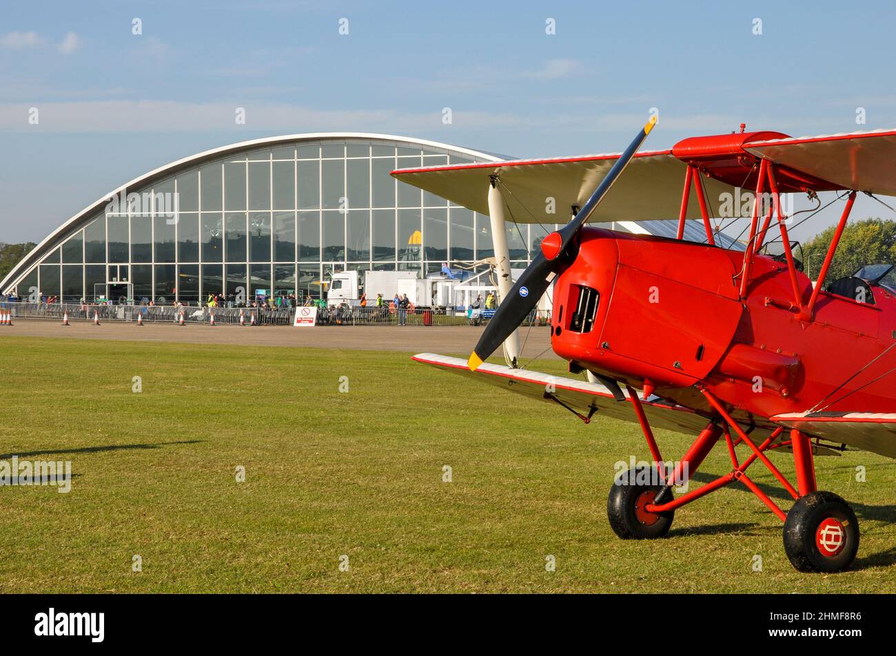 Tiger Moth biplane sitting on the grass at Duxford airfield by American Air Museum hangar. de Havilland DH82 Tiger Moth plane. Vintage aircraft Stock Photo