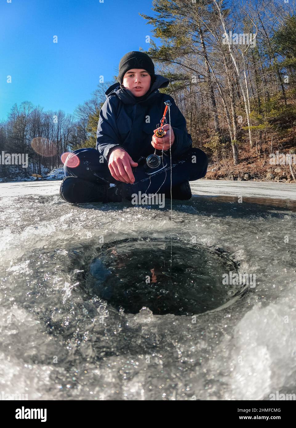 Teen boy ice fishing on a frozen lake on a cold winter day in Canada. Stock Photo