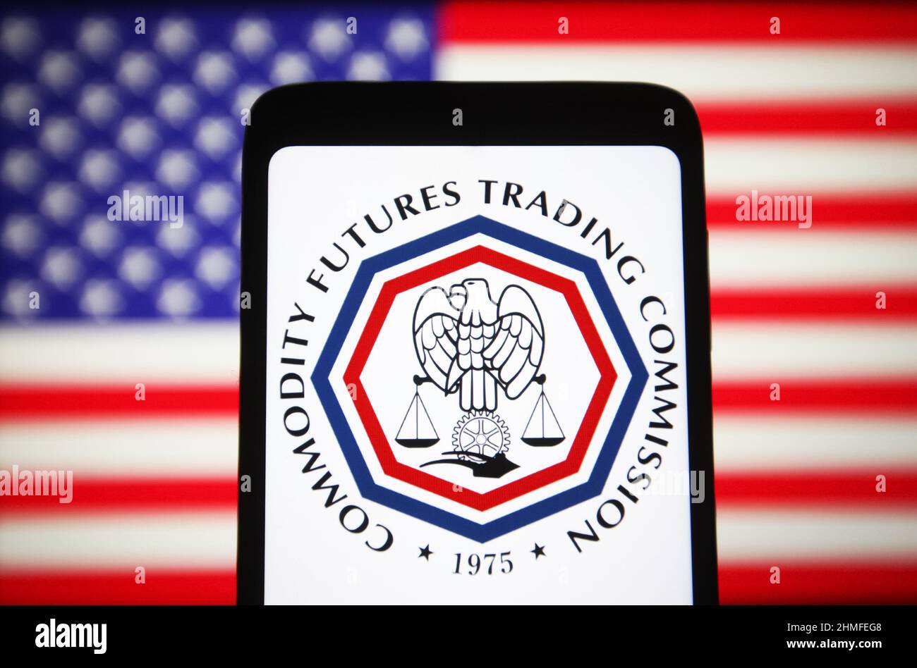 In this photo illustration, Commodity Futures Trading Commission (CFTC) logo is seen on a smartphone screen and the U.S. flag in the background. Stock Photo