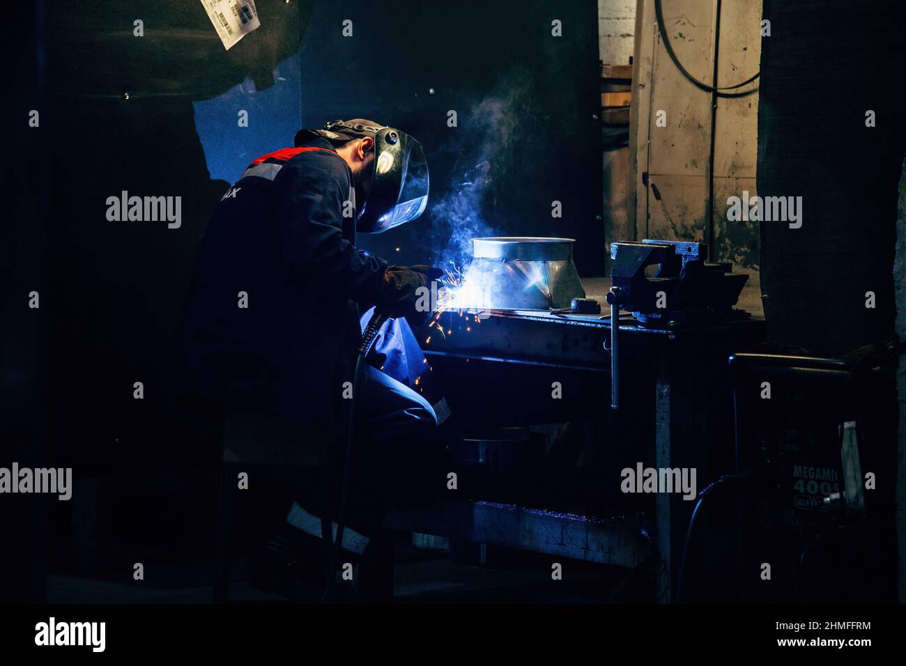 Factory worker in protective mask welding iron parts, close up. Stock Photo