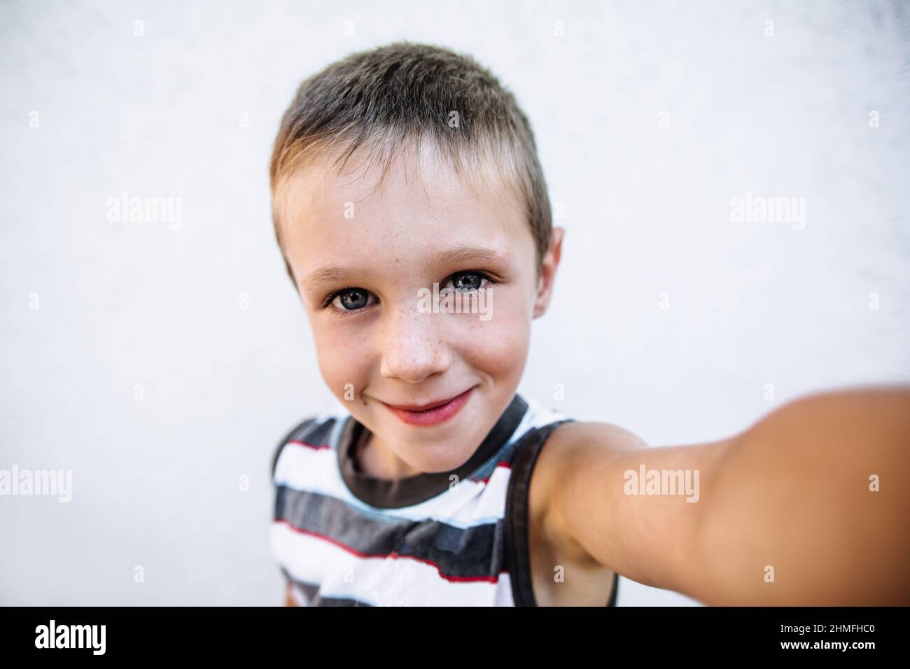 Boy with freckles in casual wear makes selfie by his hand, boy looking in camera and smiling Stock Photo