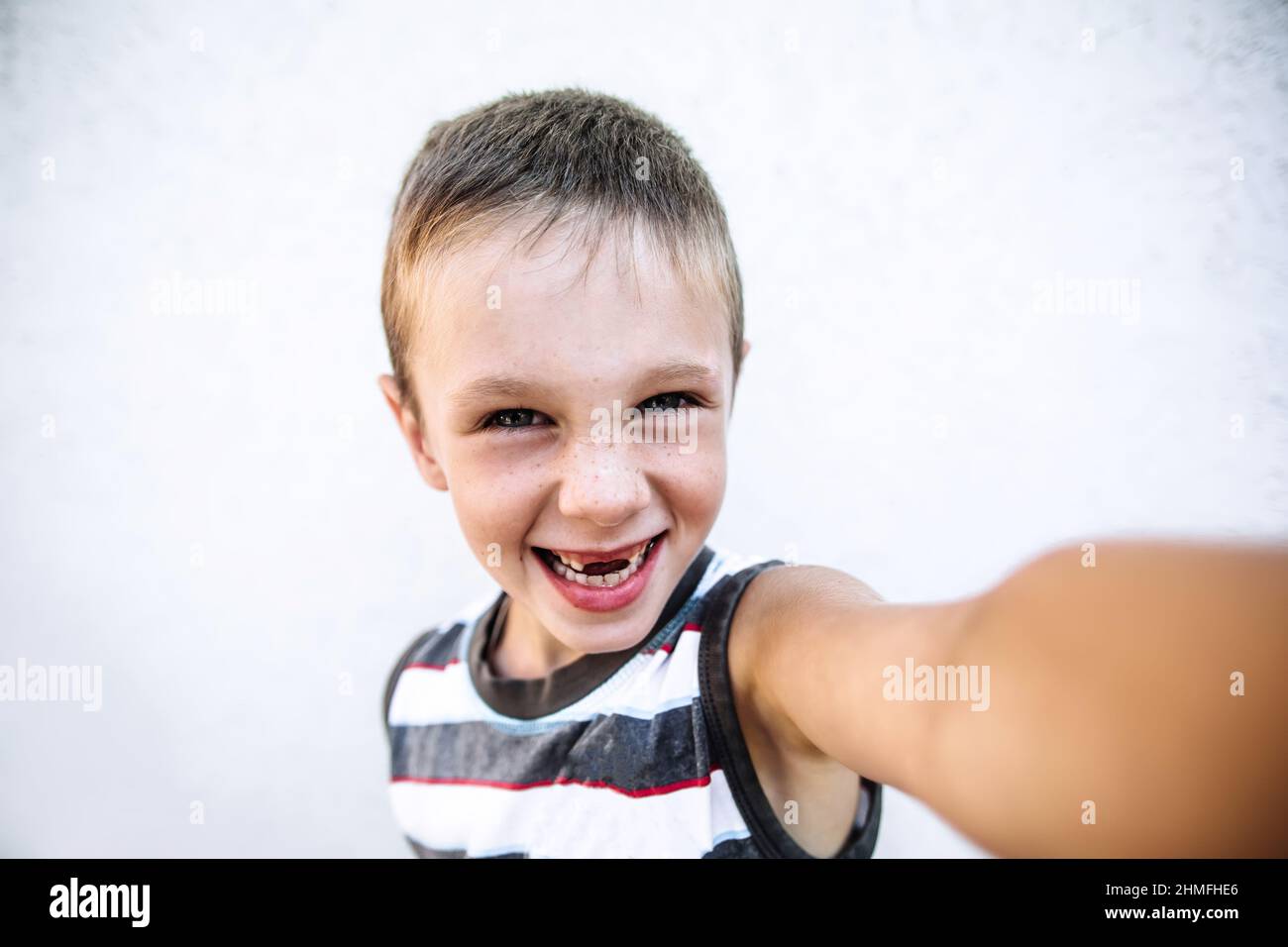 Boy with freckles without two teeth in casual wear makes selfie by his hand, boy looking in camera and smiling Stock Photo