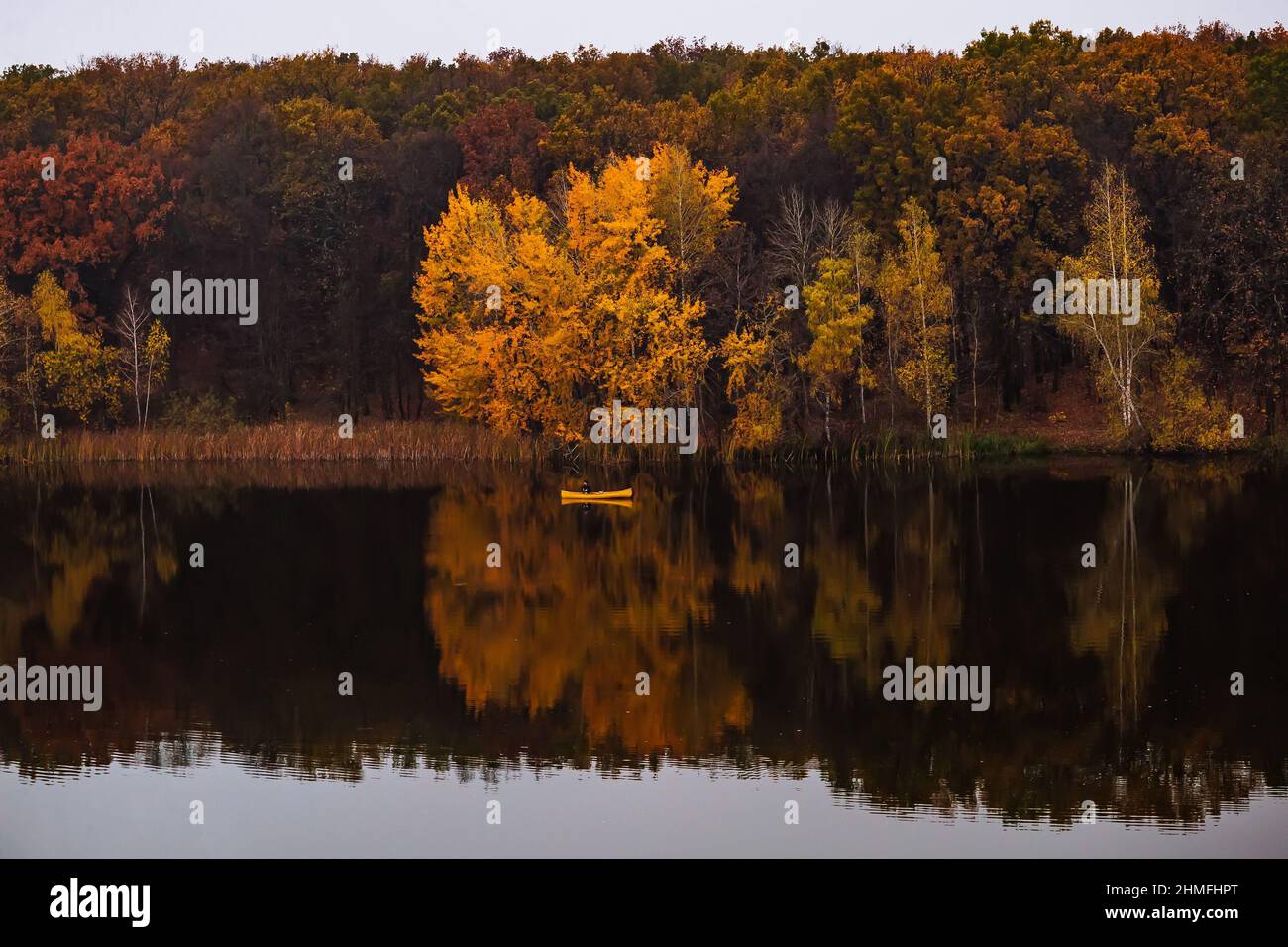 Yellow small boat near the forest with golden autumn trees, reflections in water Stock Photo