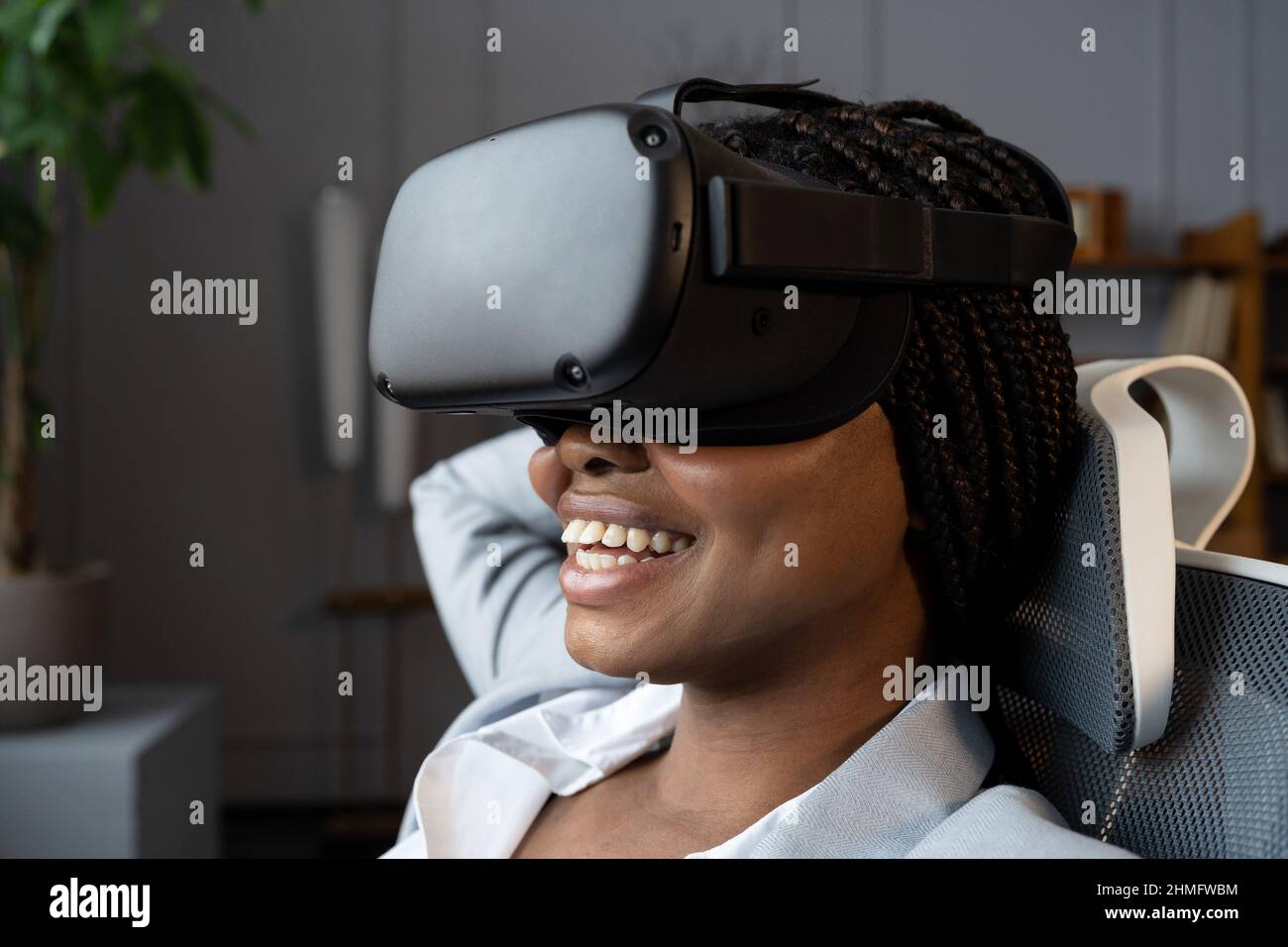 Happy relaxed afro woman in VR googles using virtual reality to relax and reduce stress at workplace Stock Photo