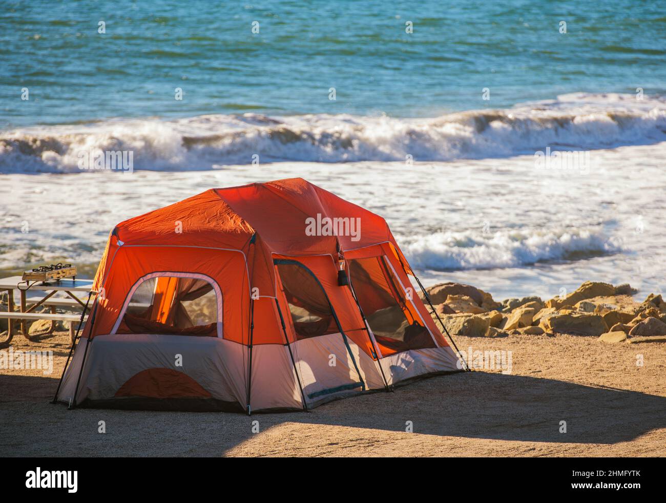 Tent Camping on the Ocean Coast. Large Modern Tent and the Water Line Right Behind. Coastal Campsite Vacation Theme. Stock Photo