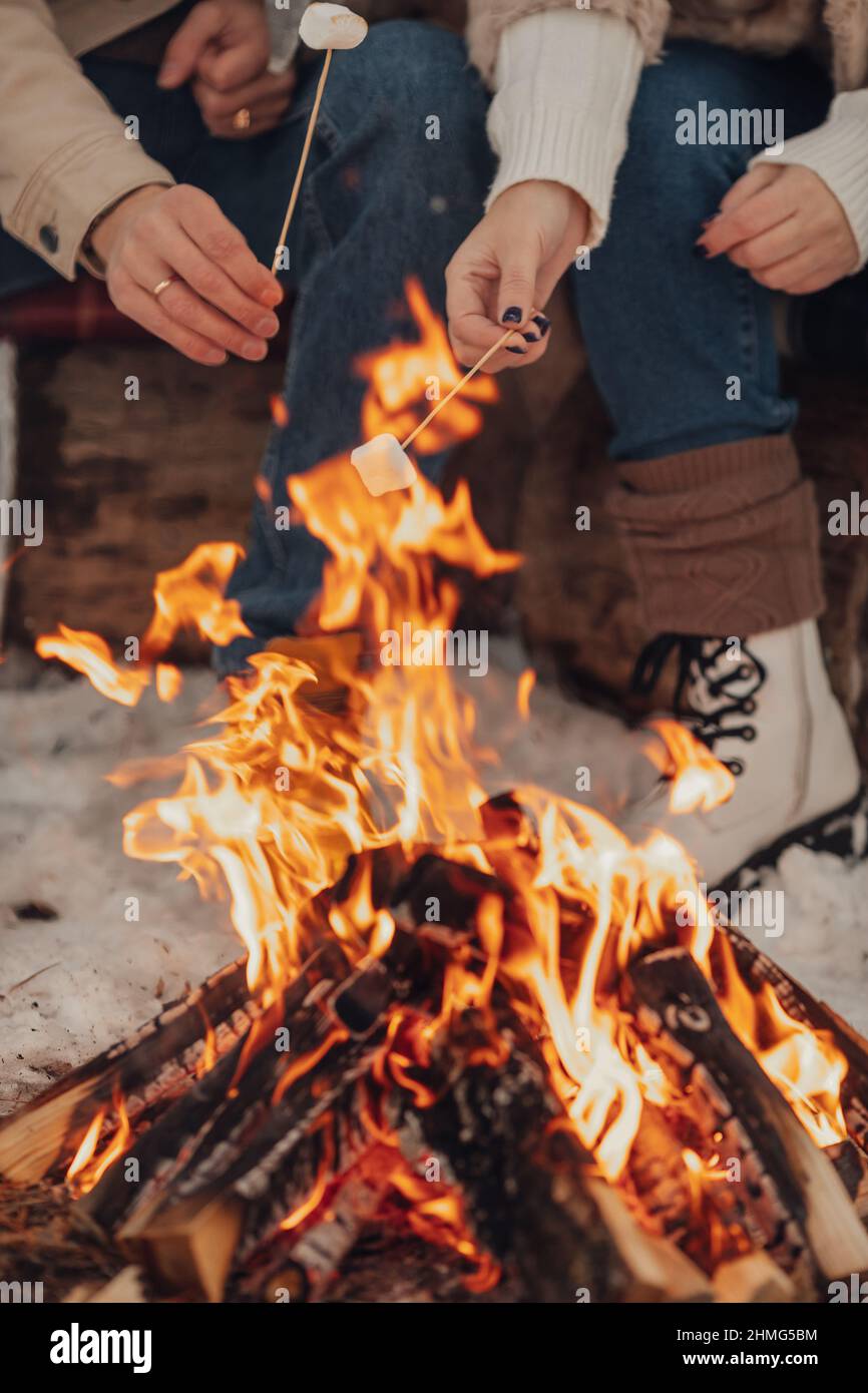 A couple in love, a man and a woman in a winter forest around a campfire drink coffee and give marshmallows Stock Photo
