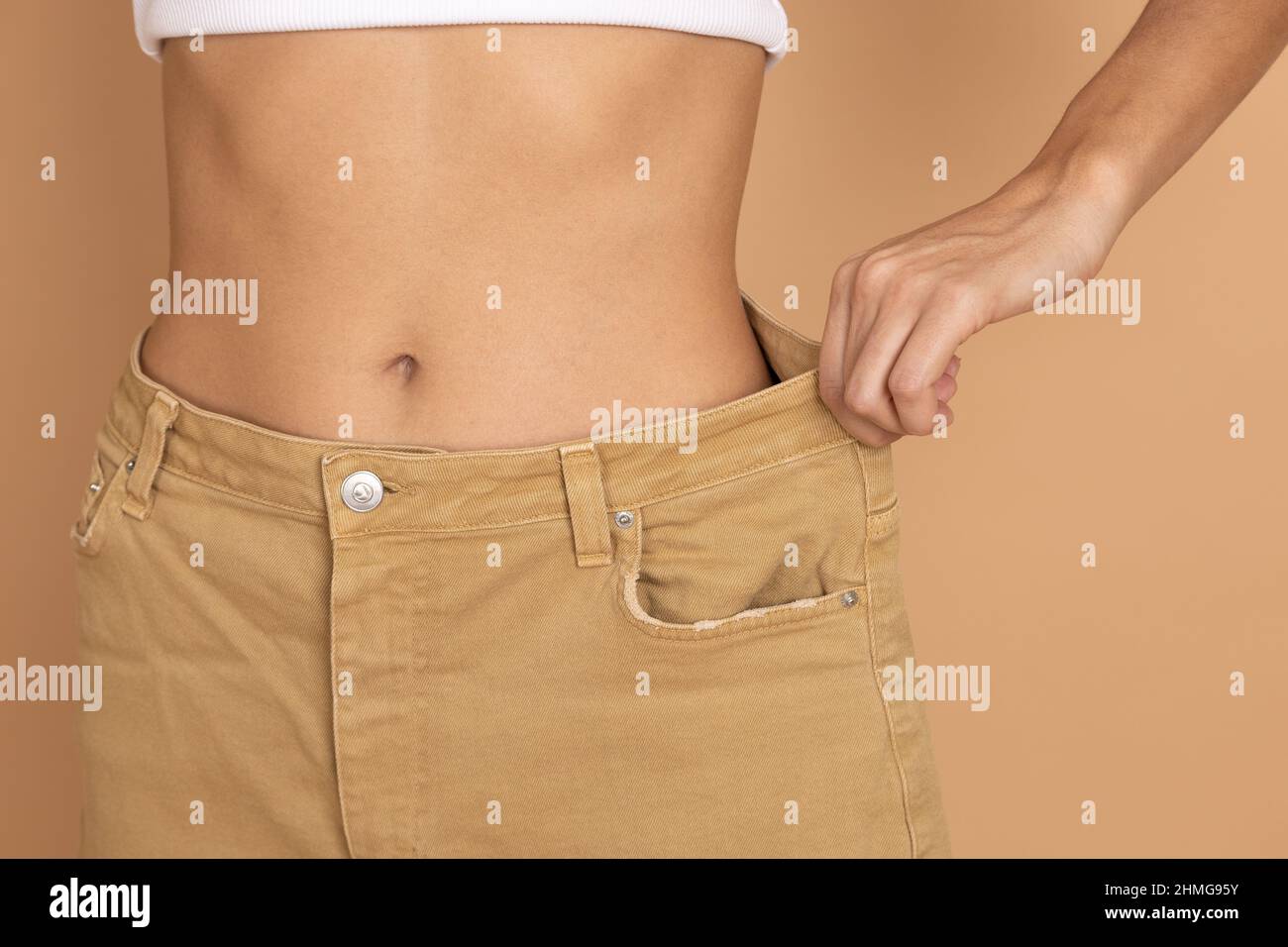 Woman with thin waist wearing big cream colored jeans on background of flesh color. Healthy eating and body building. Loosing weight by keeping diet Stock Photo