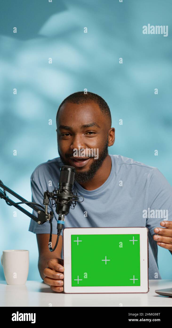 Black vlogger showing tablet with horizontal green screen on camera for podcast. African