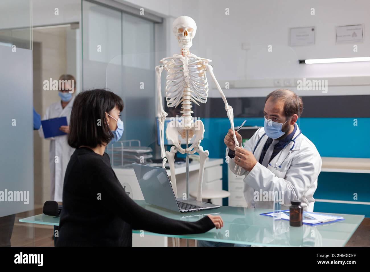 Orthopedic doctor explaining bones pain on human skeleton to patient in ...