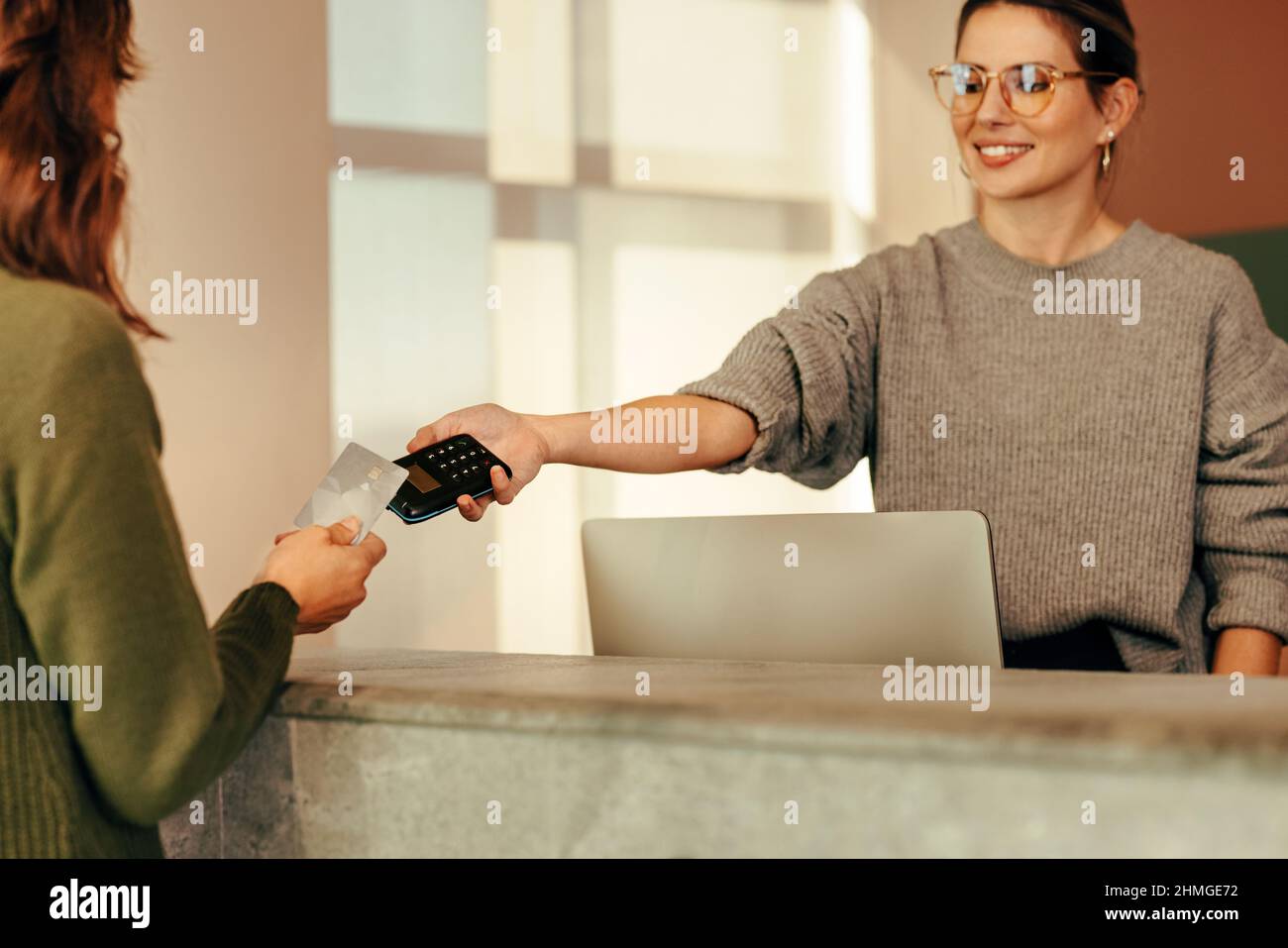 Shop assistant taking a credit card payment from a female customer. Happy small business owner smiling cheerfully while assisting her customer at the Stock Photo