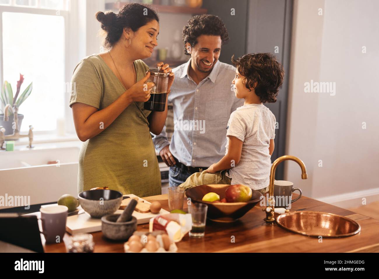 Two loving parents spending some quality time with their son in the kitchen. Mom and dad smiling while talking to their son at breakfast time. Happy e Stock Photo