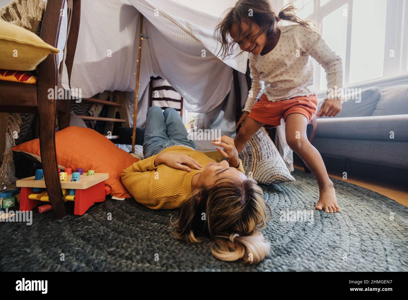 Active little girl playing with her mom in their play area. Happy young girl laughing with her mother during playtime. Mother and daughter spending so Stock Photo