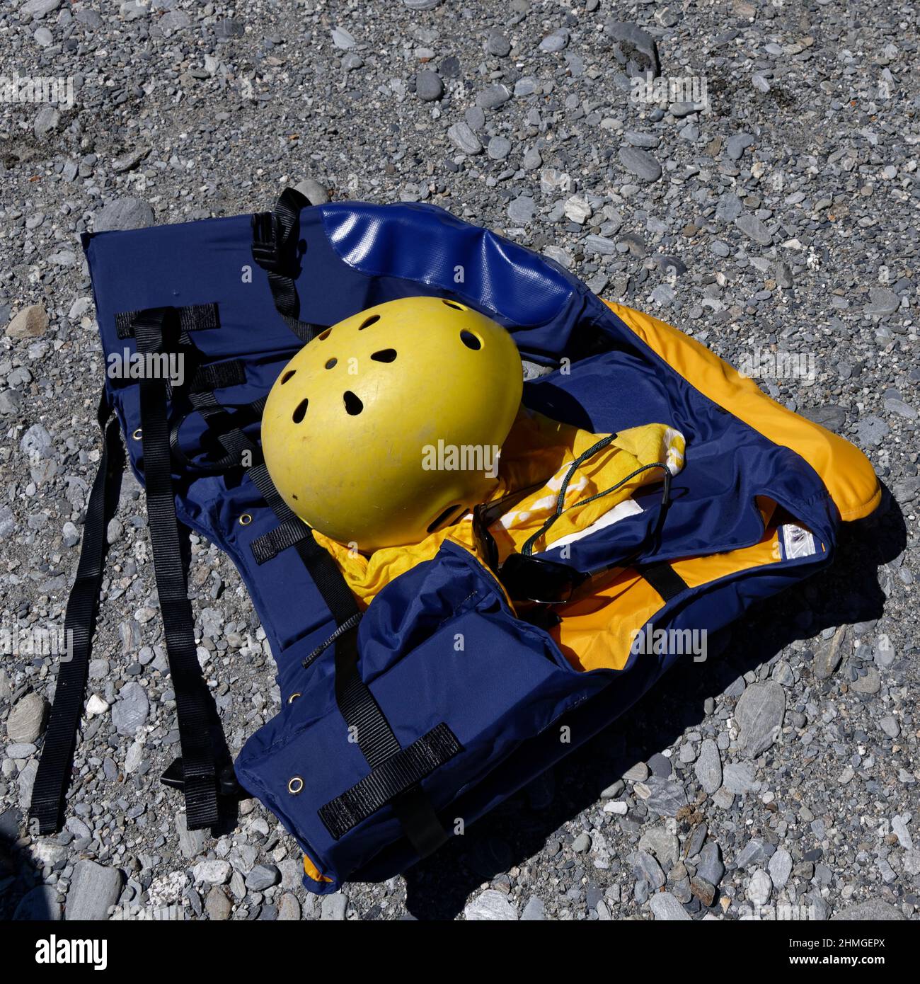 A yellow rafting helmet is on top of a life jacket on a stony river bed. Stock Photo