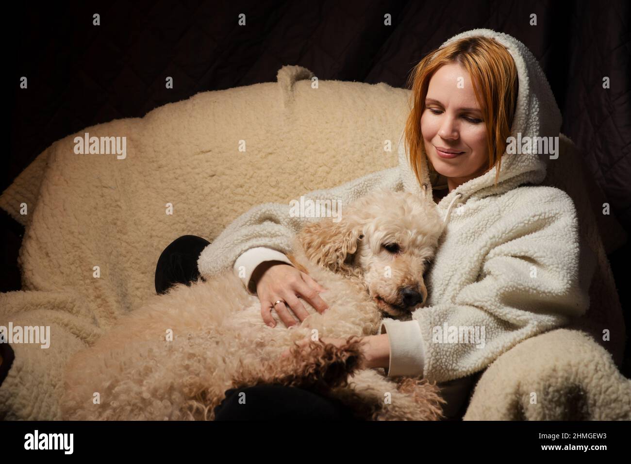 woman lies with a large dog on the couch. The shaggy domestic dog laid its head. The relationship of animals and people at home. Stock Photo