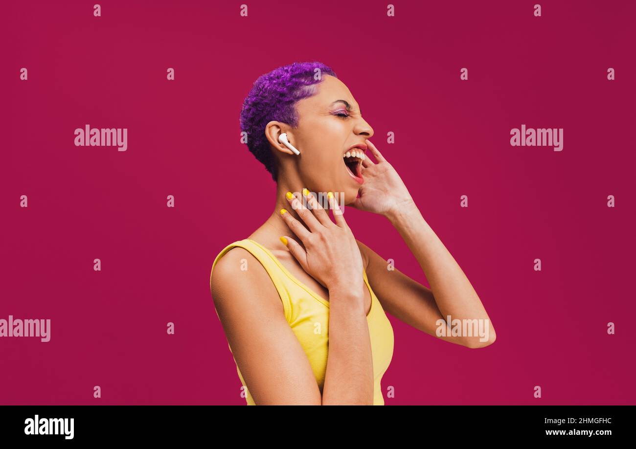 Singing along to my favourite songs. Carefree young woman listening to music on her wireless earphones. Woman with purple hair singing out loud agains Stock Photo