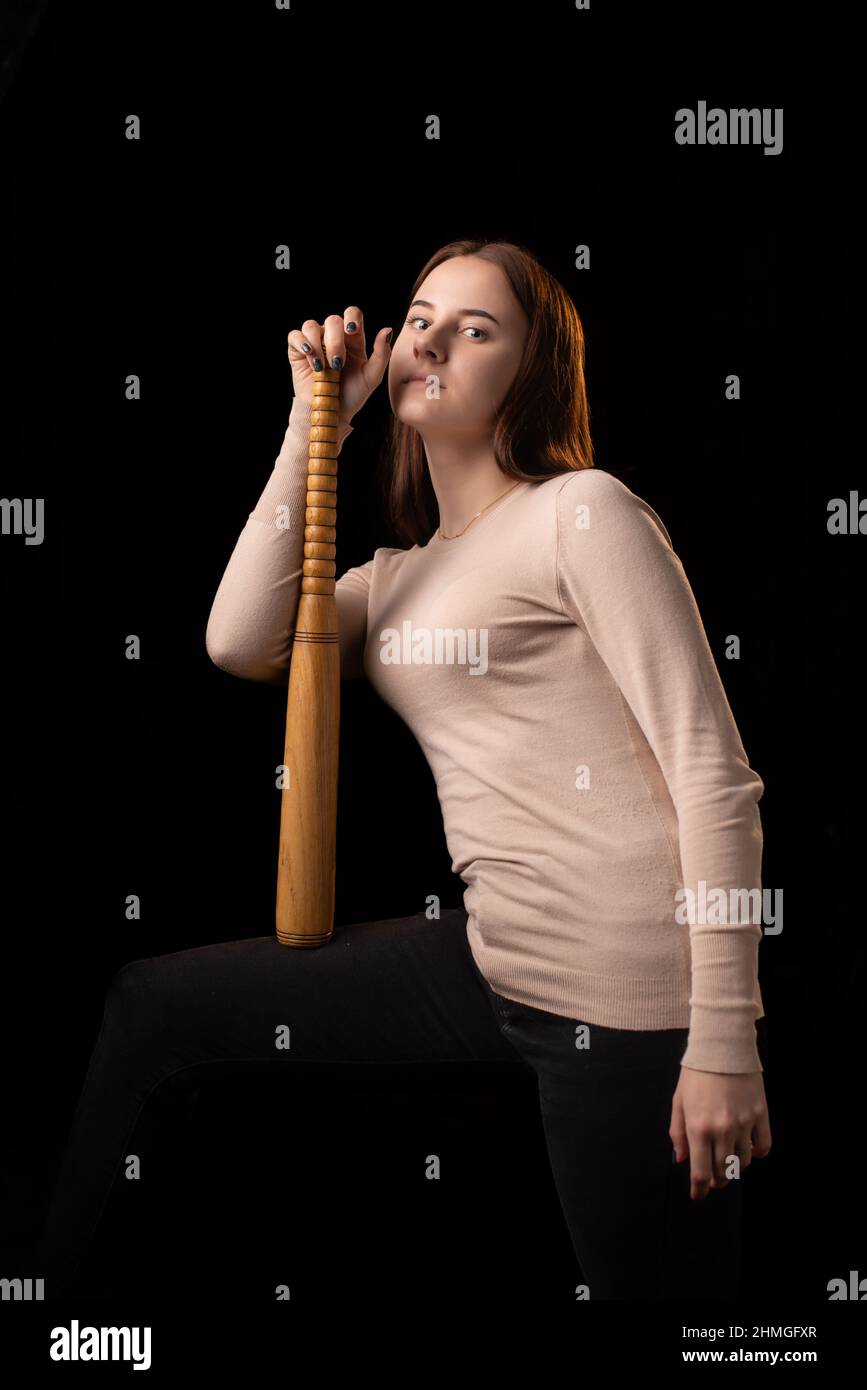 A young woman holds a bat in her hands and calmly looks into the camera