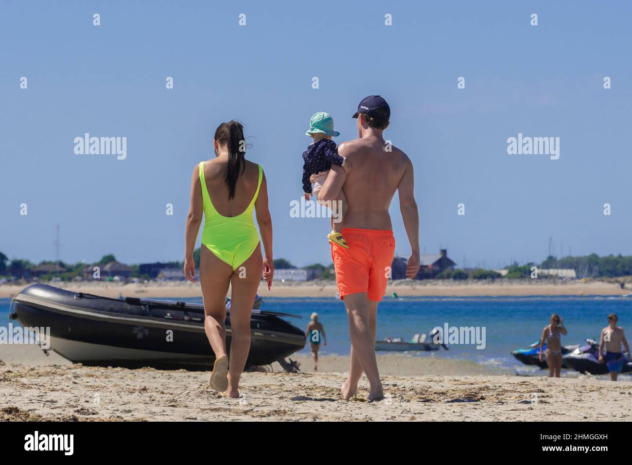 Couple with baby strolling on a hot day at West Wittering beach with a view of Hayling Island in the distance - near Chichester, West Sussex, England Stock Photo