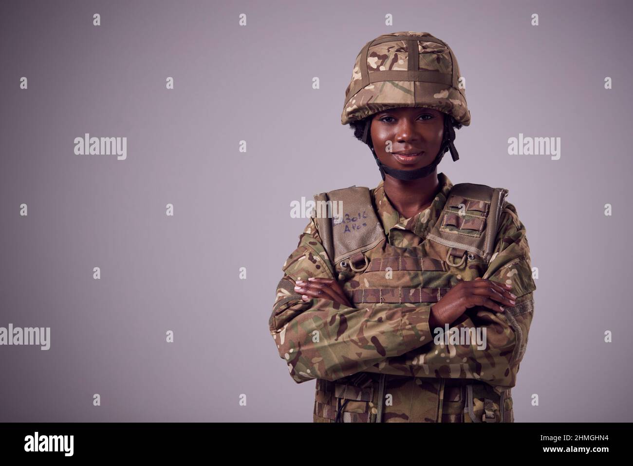 Studio Portrait Of Smiling Young Female Soldier In Military Uniform Against Plain Background Stock Photo