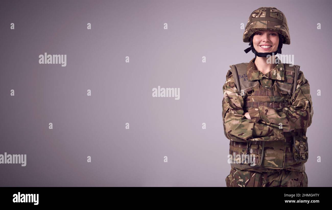 Studio Portrait Of Smiling Young Female Soldier In Military Uniform Against Plain Background Stock Photo