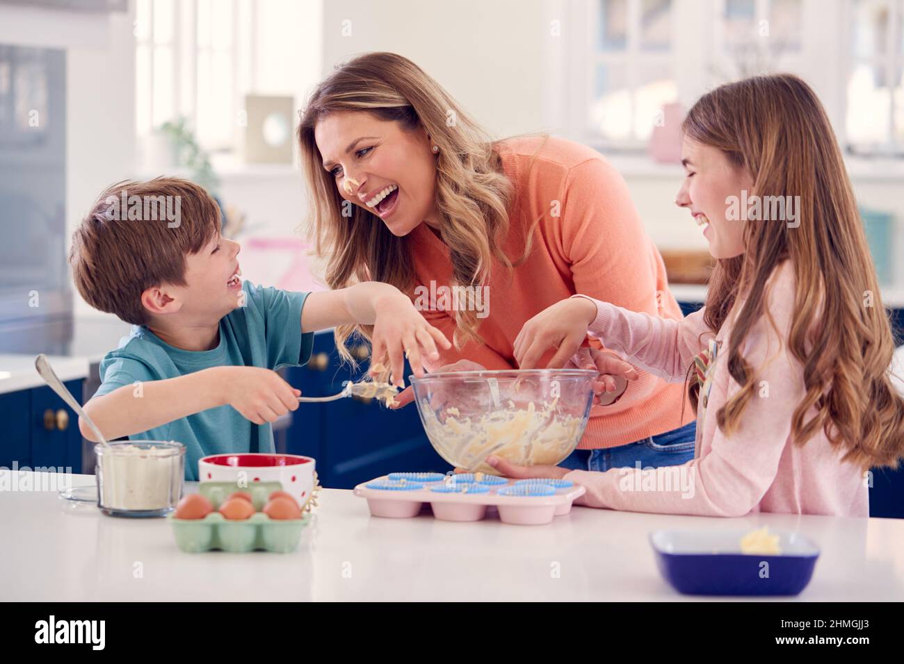 Children Putting Cake Mixture On Mother's Nose In Kitchen As They Have Fun Baking Cakes Together Stock Photo