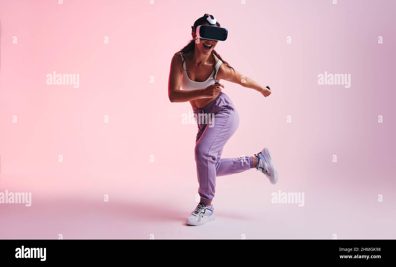 Happy young woman enjoying a virtual reality experience in a studio. Sporty young woman smiling cheerfully while wearing a virtual reality headset. At Stock Photo