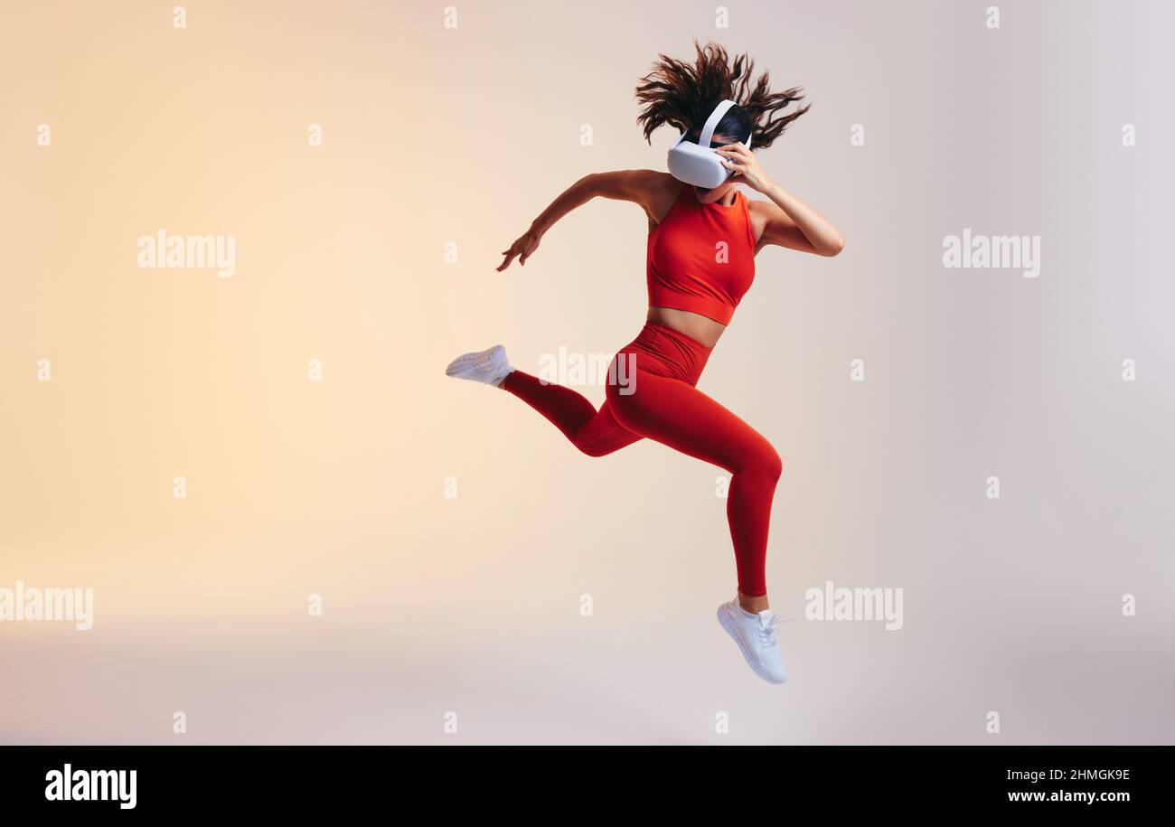 Sporty young woman sprinting while wearing a virtual reality headset. Athletic young woman running during a virtual training session. Woman working ou Stock Photo